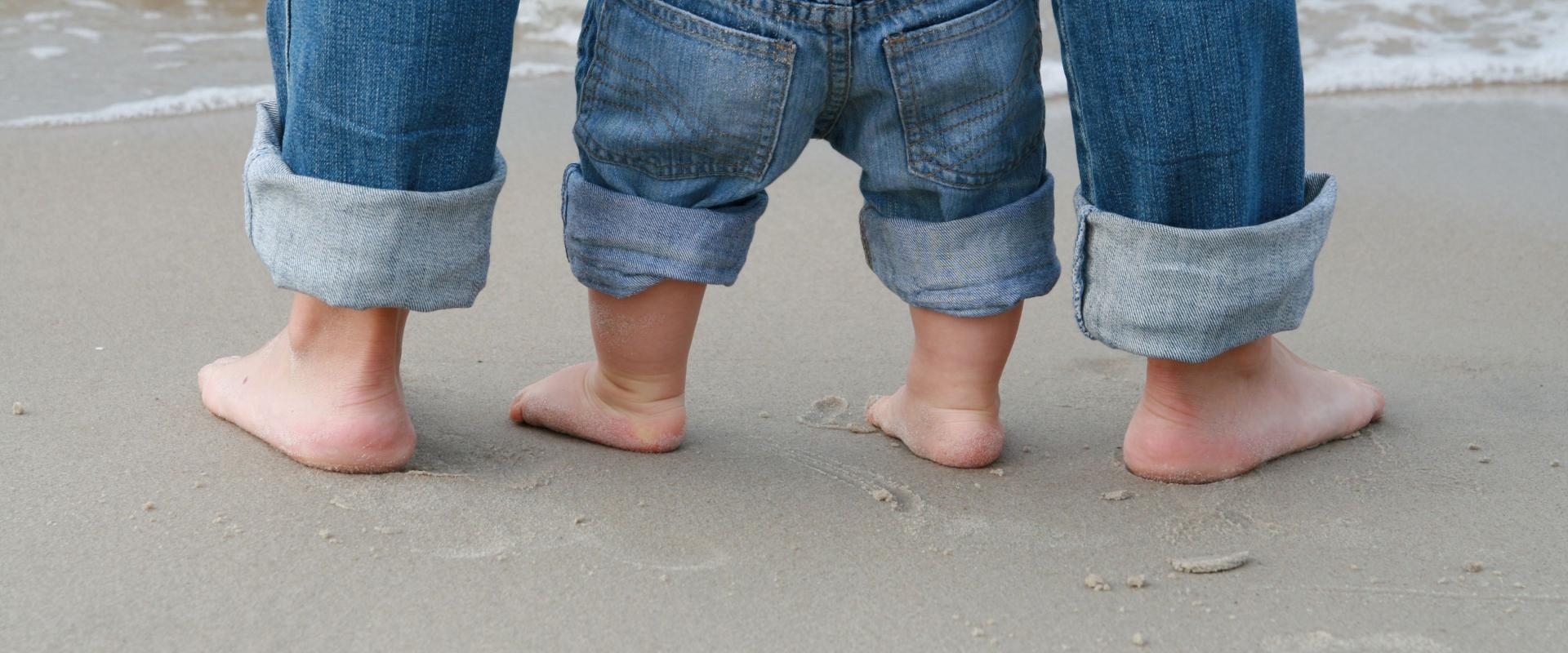 Füße einer erwachsenen Person und eines Kleinkindes im Sand