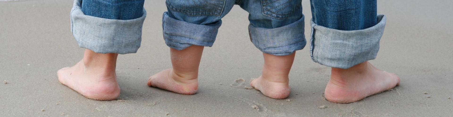 Füße einer erwachsenen Person und eines Kleinkindes im Sand