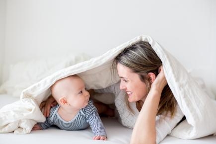 Ein Kleinkind und eine Frau unter einer Bettdecke, sie lächeln sich an