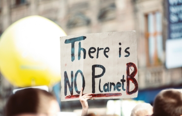 Jemand hält ein Stück Karton hoch. Darauf steht "There is NO Planet B".
