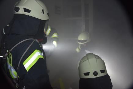 Vier Feuerwehrleute in dunklem Raum voller Qualm
