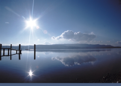 Steg im Bodensee bei der Halbinsel Mettnau, im Wasser spiegeln sich Sonne und Wolken