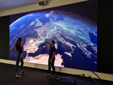 Eine Frau und ein Mann stehen vor einer Darstellung von grünen Datenströmen auf einer virtuellen Erdkugel