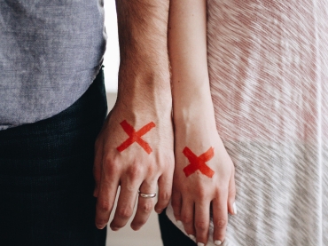 Zwei Hände mit Eheringen und roten Kreuzen auf der Hand 