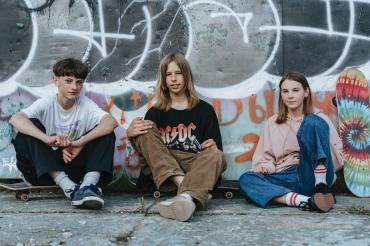 drei Jugendliche sitzen vor einer Wand mit Skateboard