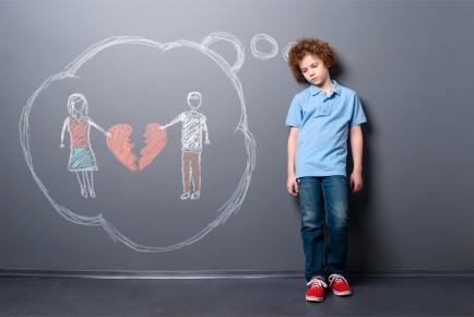 Ein Kind steht vor einer grauen Wand. Mit Kreide ist dort eine Denkblase aufgemalt, in der ein Mann, eine Frau und zwischen ihnen ein gebrochenes Herz zu sehen sind. 