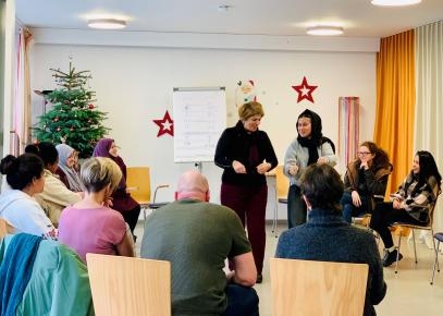 Mehrere Personen in einem Stuhlkreis. Zwei Personen stehen in der Mitte .