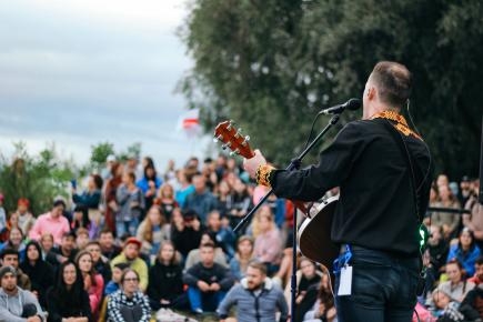 Symbolbild: Mann mit Gitarre und Mikrofon vor Publikum