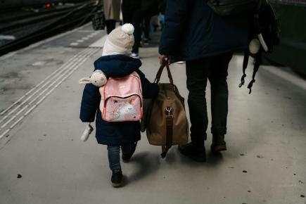 Symbolbild: von hinten kleines Kind mit Mütze und pinkem Rucksack an der Hand von erwachsener Person