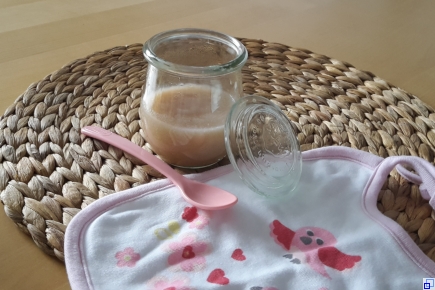 Symbolbild: Babylatz, Kinderplastiklöffel und Weckglas mit Inhalt auf Tisch